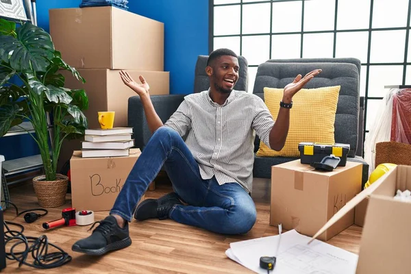 stock image African american man sitting on the floor at new home smiling showing both hands open palms, presenting and advertising comparison and balance 