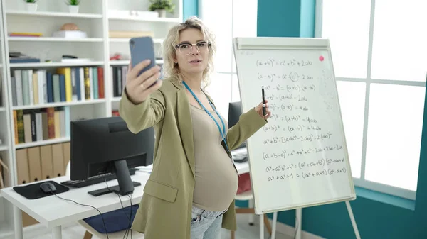 Young pregnant woman teaching online maths lesson on magnetic board at classroom