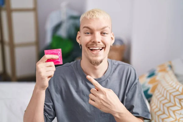 Young Caucasian Man Holding Condom Sitting Bed Smiling Happy Pointing — Stock Photo, Image