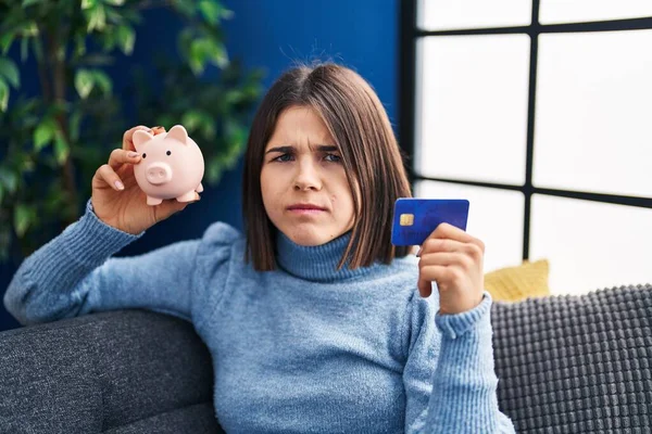 Mulher Hispânica Jovem Segurando Banco Porquinho Cartão Crédito Cético Nervoso — Fotografia de Stock