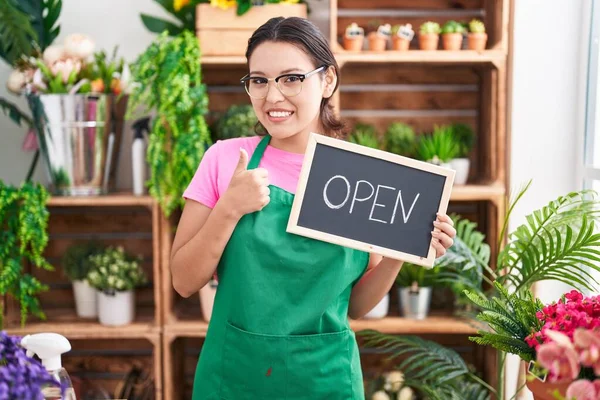 Hispanic young woman working at florist holding open sign smiling happy and positive, thumb up doing excellent and approval sign