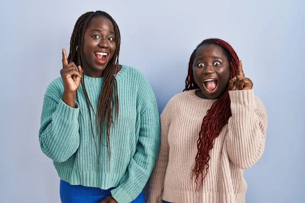 2人のアフリカ人女性が成功したアイデアで指を指して青い背景に立っています 興奮して幸せよ 第1位 — ストック写真