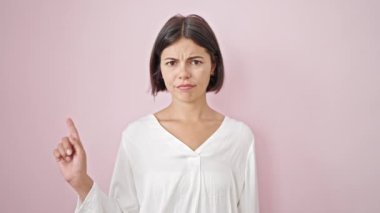 Genç, güzel İspanyol bir kadın, izole edilmiş pembe arka planda kızgın yüzüyle boş bir alanı işaret ediyor.