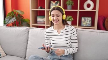 Genç, güzel İspanyol kadın müzik dinliyor ve dans ediyor. Evdeki kanepede oturuyor.