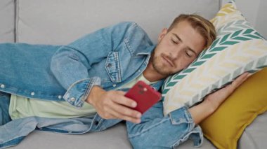 Kafkasyalı genç adam akıllı telefon kullanıyor. Kanepede uzanıyor ve evde uyuyor.