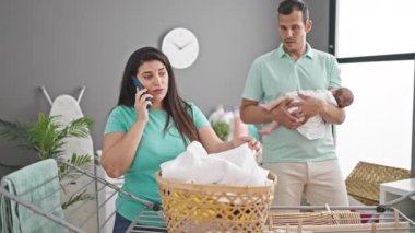 Çamaşır odasında akıllı telefon kullanarak çamaşır ipine asılan üç kişilik bir aile.