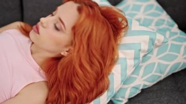 Young redhead woman using smartphone lying on sofa at home