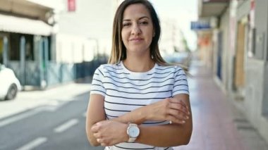 Orta Doğulu bir kadın sokakta çapraz kollarla gülümsüyor.