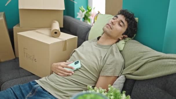 Jovem Hispânico Homem Dormindo Sofá Segurando Smartphone Nova Casa — Vídeo de Stock