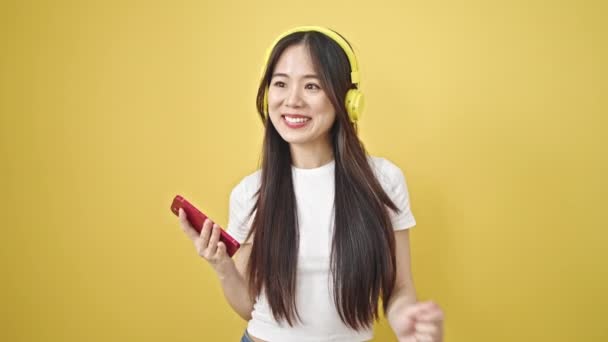 Junge Chinesin Tanzt Mit Kopfhörern Über Smartphone Vor Isoliertem Gelben — Stockvideo