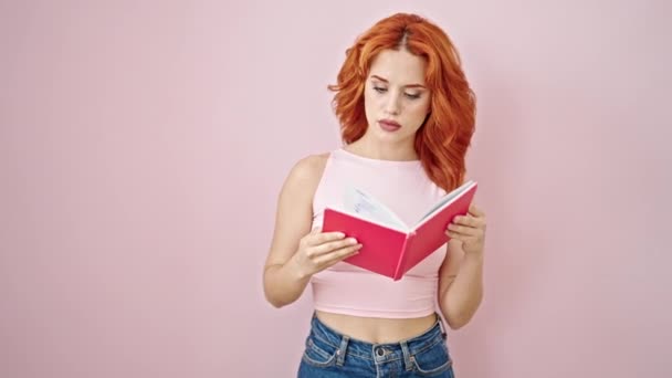 Jonge Roodharige Vrouw Lezen Boek Kijken Boos Geïsoleerde Roze Achtergrond — Stockvideo