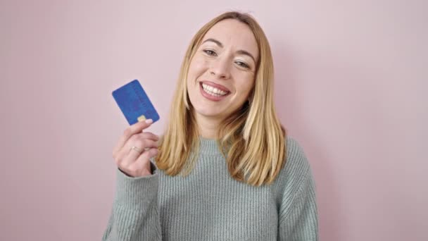 Jovem Loira Sorrindo Confiante Segurando Cartão Crédito Sobre Fundo Rosa — Vídeo de Stock