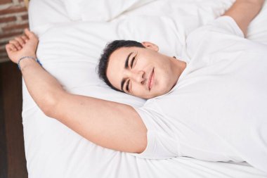 Young hispanic man waking up stretching arms at bedroom