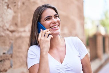 Gülümseyen genç bir kadın caddedeki akıllı telefondan konuşuyor.