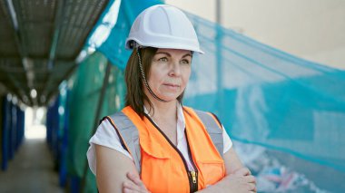 Orta yaşlı İspanyol kadın inşaatçı inşaat alanında çapraz kollarla duruyor.