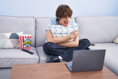 Laptopta korku filmi izleyen İspanyol genç adam kameraya seksi bir ifadeyle bakıyor, neşeli ve mutlu bir yüzle.. 