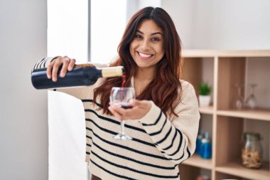 Young hispanic woman smiling confident pouring wine on glass at home