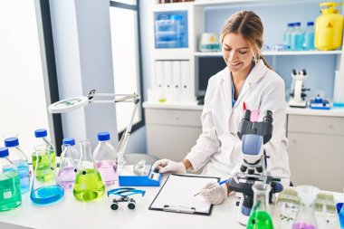 Young hispanic woman scientist weighing diamond writing report at laboratory