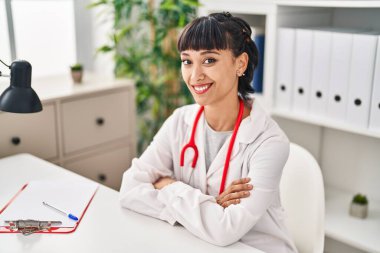 Klinikteki masada oturan, doktor üniforması giyen genç bir kadın.