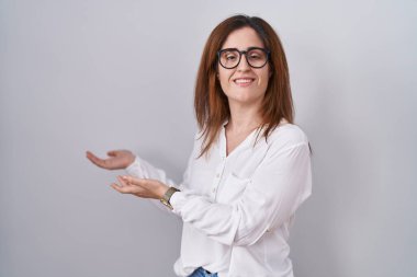 Esmer kadın, izole edilmiş beyaz arka planda duruyor ve gülümseyerek içeri girmeye davet ediyor. 