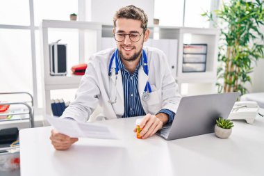 Young man doctor reading medical report holding pills at clinic