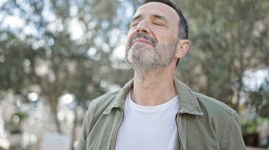 Orta yaşlı bir adam parkta gözleri kapalı nefes alıyor.