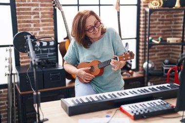 Müzik stüdyosunda ukulele çalarken gülümseyen son sınıf bayan müzisyen.