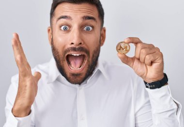 Yakışıklı İspanyol adam Monero kripto bozuk para tutuyor zaferi mutlu bir gülümsemeyle kutluyor ve kazanan el kaldırarak ifade ediyor 