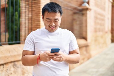 Young chinese man smiling confident using smartphone at street