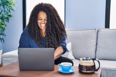 African american woman using laptop drinking coffee at home