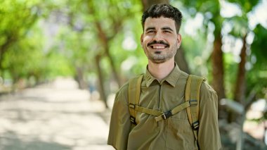 Sırt çantalı genç İspanyol turist parkta gülümsüyor.
