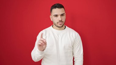 Genç İspanyol adam, izole edilmiş kırmızı arka planda parmak ile hayır diyor.
