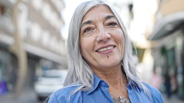 Orta yaşlı, kır saçlı, gülümseyen, kendine güvenen bir kadın.