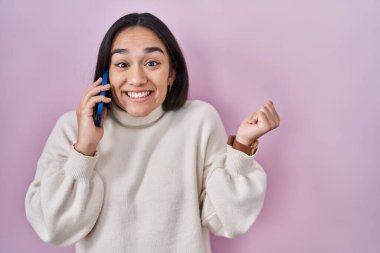 Genç Güney Asyalı kadın akıllı telefondan konuşuyor gururla bağırıyor, zaferi kutluyor ve başarıyı kollarını kaldırarak kutluyor. 
