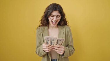 Young beautiful hispanic woman smiling confident counting dollars over isolated yellow background