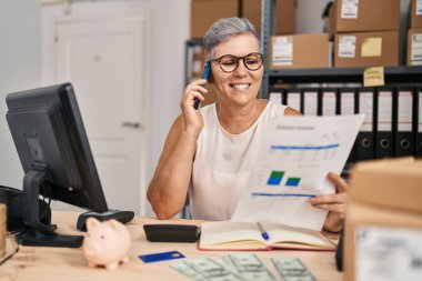 Middle age woman ecommerce business worker talking on the smartphone at office