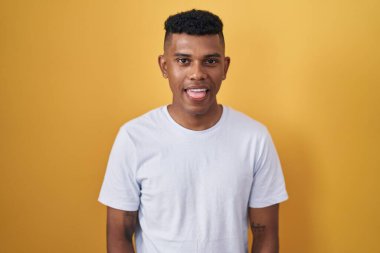 Sarı arka planda dikilen İspanyol genç adam komik bir ifadeyle mutlu bir şekilde dilini dışarı çıkarıyor. duygu kavramı. 