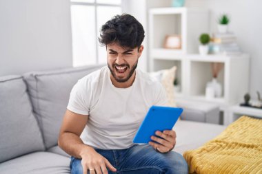 Sakallı İspanyol bir adam kanepeye oturmuş sinirli ve sinirli sinirli sinirli sinirli bağırıyor ve öfkeyle bağırıyor. öfke ve agresif konsept. 