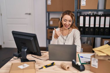 Küçük işletme şirketinde çalışan İspanyol kadın, kulaklık takıyor, gülümsüyor, mutlu ve pozitif, başparmağıyla mükemmel ve onay işareti yapıyor. 