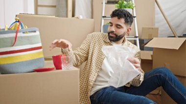 Young hispanic man packing cardboard box at new home