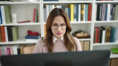 Young beautiful hispanic woman student using computer studying at library university