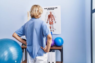 Young blond man pysiotherapist standing on back view at rehab clinic
