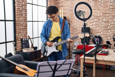 Young hispanic man musician playing electrical guitar recording video at music studio