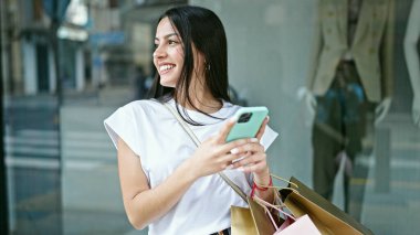 Genç ve güzel İspanyol kadın elbise mağazasında akıllı telefon kullanıyor.