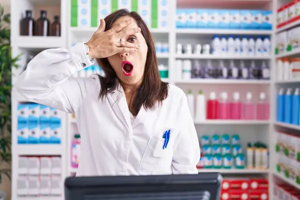 中年ブルネット女性仕事で薬局ドラッグストアPeekingでショックカバー顔と目と手で 恥ずかしい表情で指を通して見る — ストック写真
