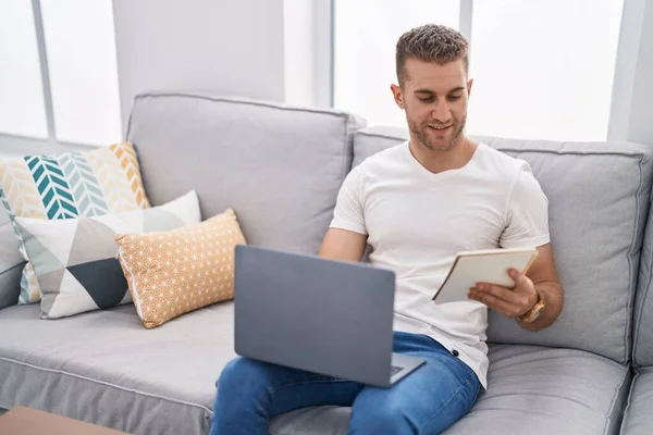 stock image Young caucasian man using laptop reading notebook at home