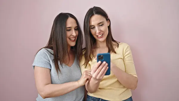 Дві Жінки Посміхаються Впевнено Використовуючи Смартфон Над Ізольованим Рожевим Тлом — стокове фото