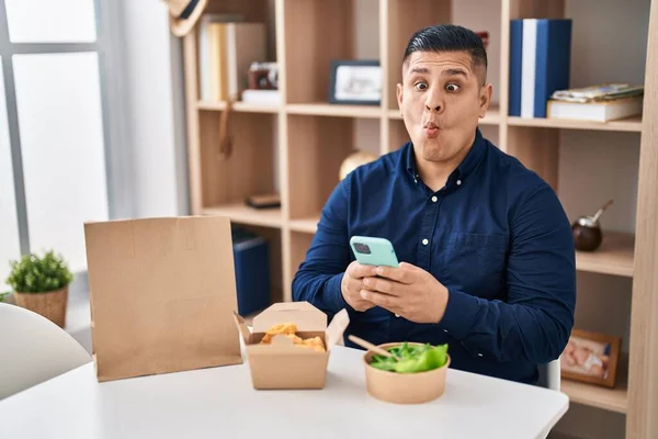 Joven Hispano Comiendo Comida Para Llevar Usando Smartphone Haciendo Cara —  Fotos de Stock