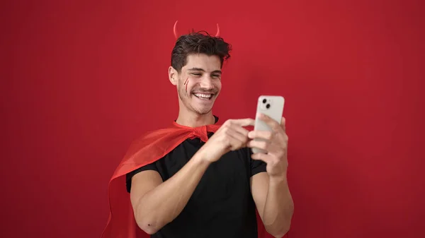 Jovem Hispânico Vestindo Traje Diabo Usando Smartphone Sobre Fundo Vermelho — Fotografia de Stock
