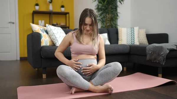 年轻的孕妇坐在瑜伽垫上 在家里摸着肚子 — 图库照片